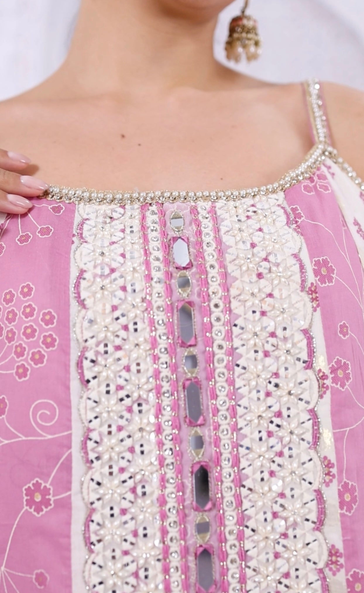 Close-up of a pink garment with intricate white embroidery and embellishments.