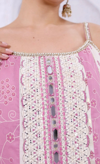 Close-up of a pink garment with intricate white embroidery and embellishments.